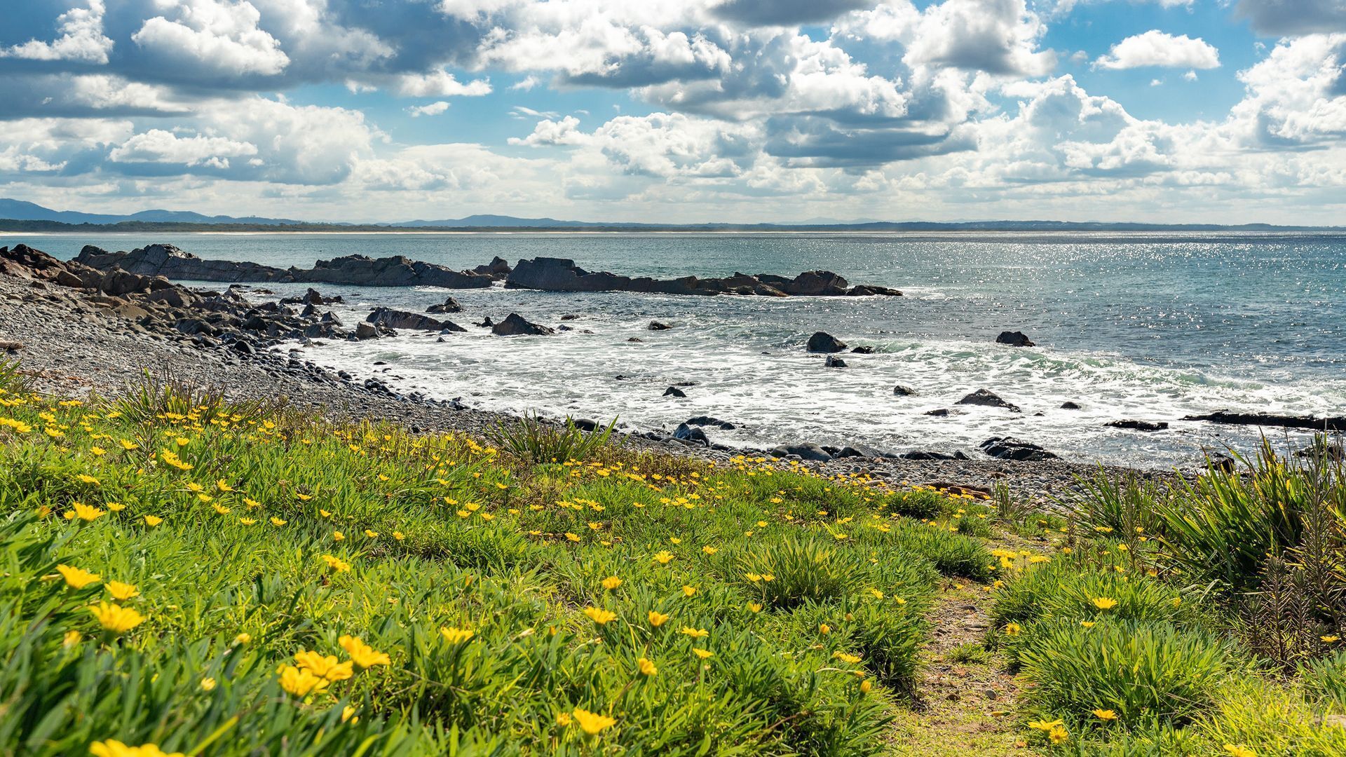 A coastal landscape with rocky shores, green vegetation, and a clear sky.