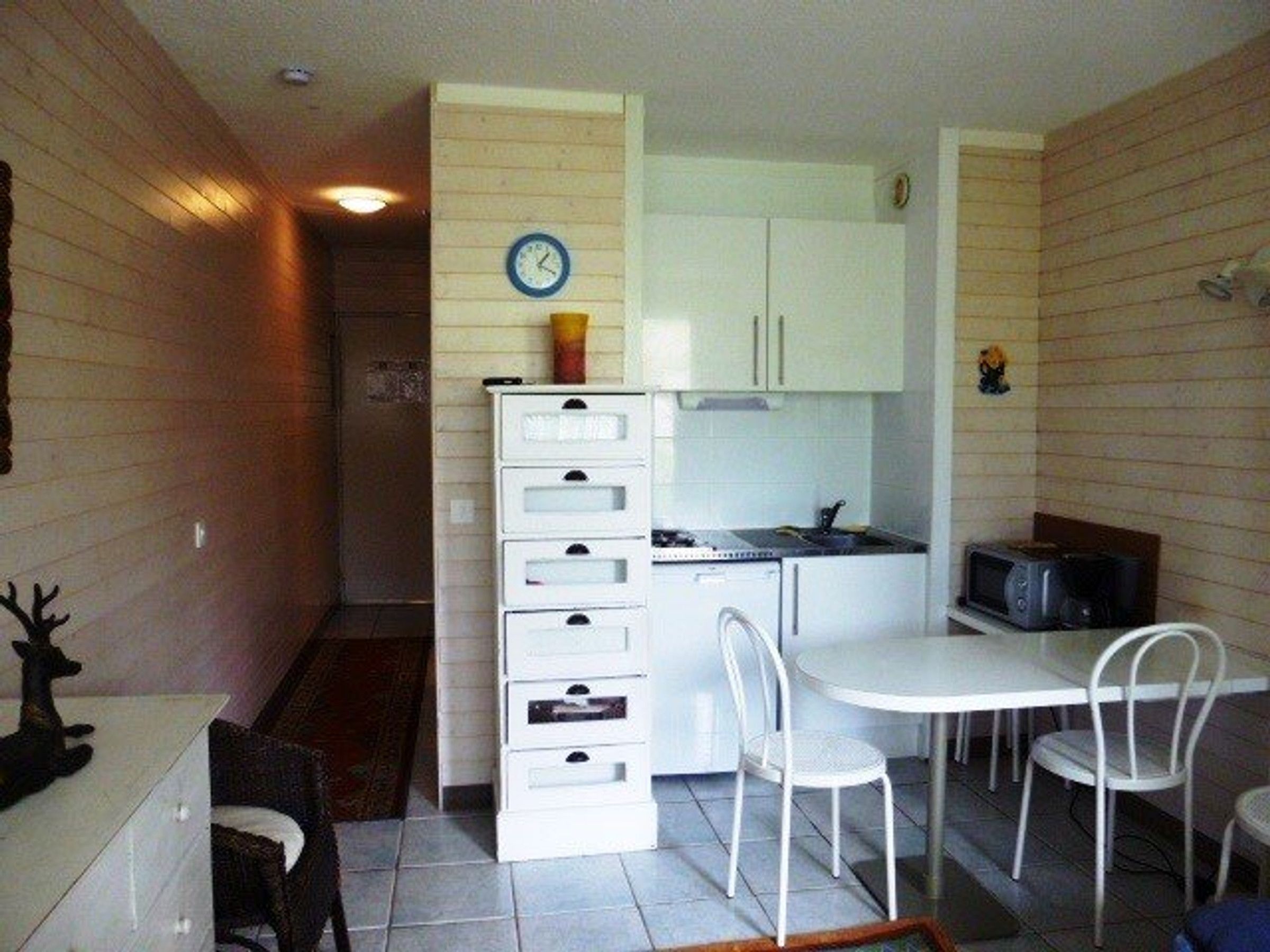 A compact kitchen with white cabinets, a microwave, and a dining area with white chairs.