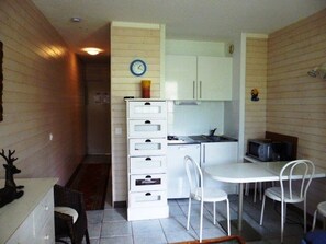 A compact kitchen with white cabinets, a microwave, and a dining area with white chairs.
