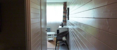 Un estrecho pasillo con paneles de madera, una silla blanca, una mesita y una alfombra en el suelo.