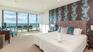 A bedroom with a large bed, a view of the sea, and a balcony with chairs.