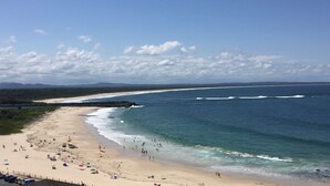 A beach with people, a rocky breakwater, and a clear sky.