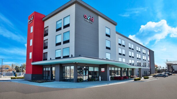 Ein modernes Hotel mit roter und grauer Fassade, großen Fenstern und einem überdachten Eingangsbereich.