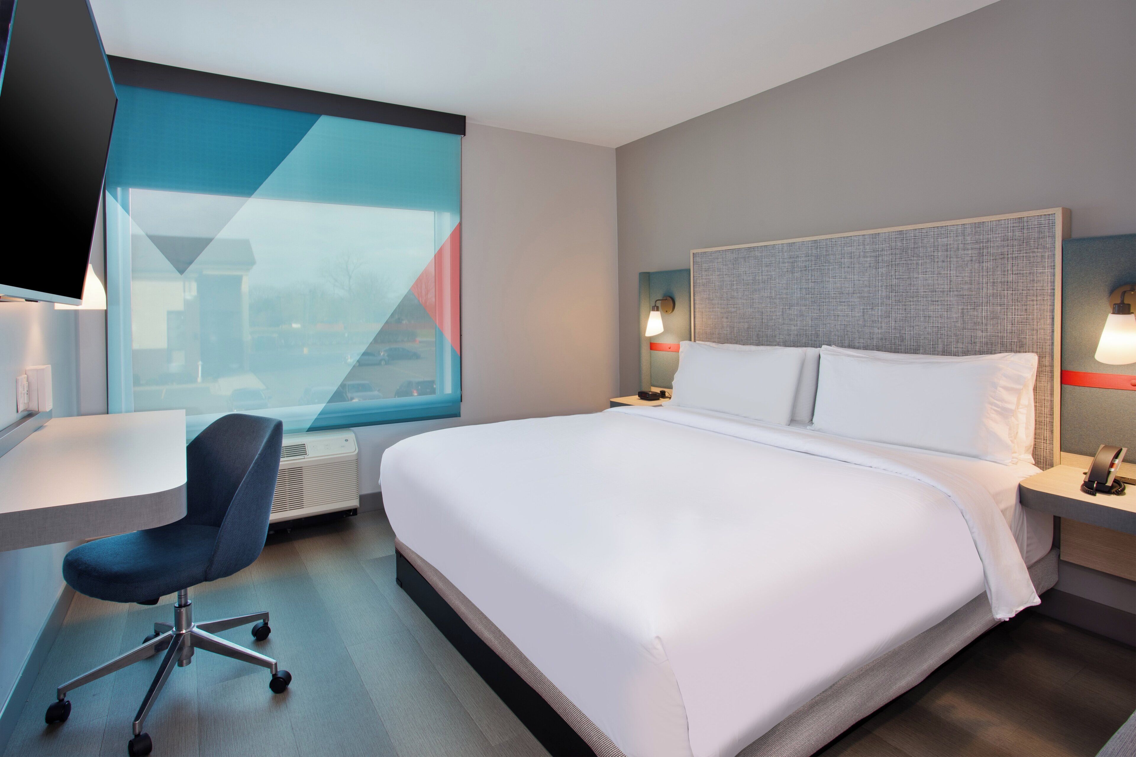 A hotel room with a large bed, a desk, a chair, and a television.