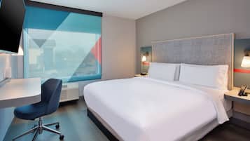 A hotel room with a large bed, a desk, a chair, and a television.