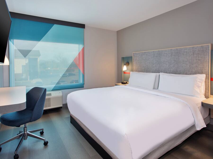 Ein Hotelzimmer mit einem großen Bett, einem Schreibtisch, einem Sessel und einem Fernseher.