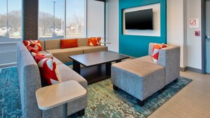 Eine moderne Lobby mit einem Ecksofa, Sesseln, einem Couchtisch und einem an der Wand befestigten Flachbildfernseher.