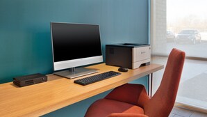 Ein moderner Schreibtisch mit einem Desktop-Computer, einem Drucker und einem roten Bürostuhl.