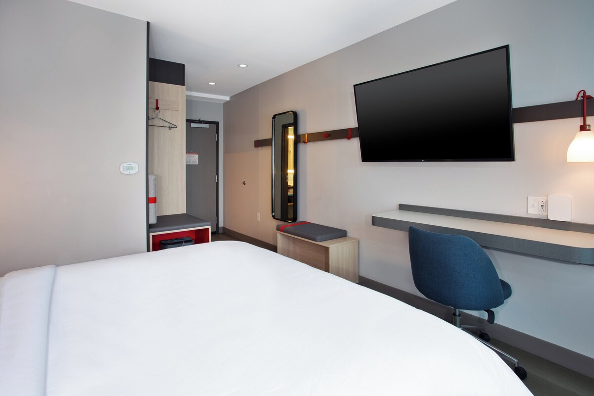 Une chambre d’hôtel équipée d’un lit, d’un bureau, d’une chaise, d’un téléviseur fixé au mur et d’un miroir.