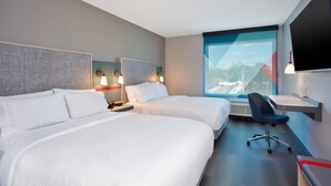 Ein Hotelzimmer mit zwei Betten, einem Schreibtisch, einem Stuhl und einem großen Fenster mit Aussicht.