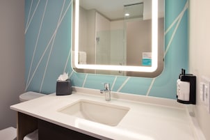 Un baño con lavamanos blanco, espejo y dispensador de toallas.