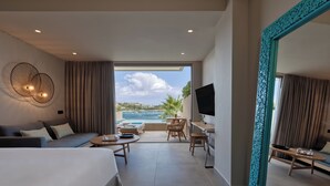 Een moderne hotelkamer met een groot bed, een zithoek met een tafel en stoelen, een televisie en een balkon met uitzicht op zee.