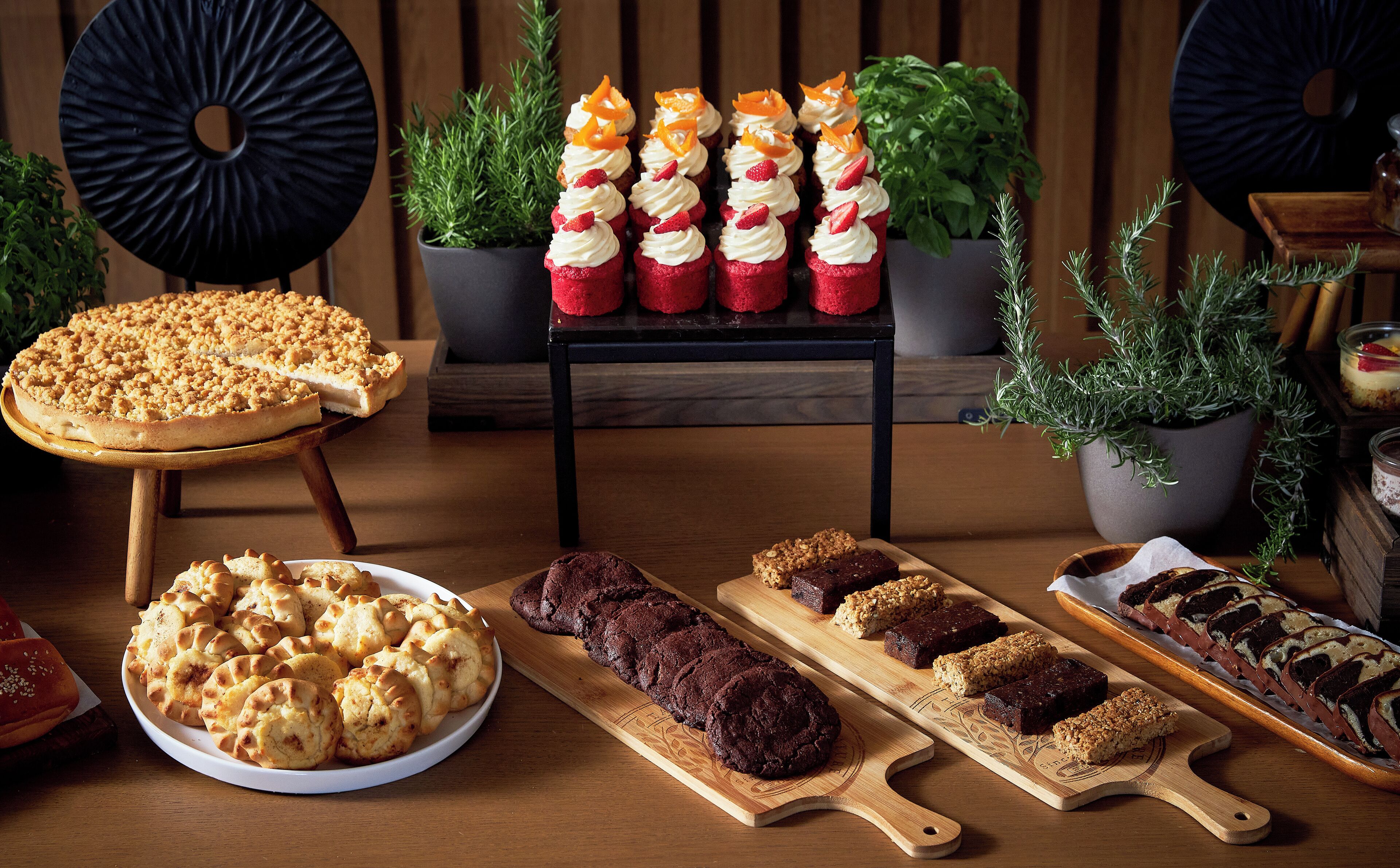 A variety of baked goods including cupcakes, a pie, and cookies displayed on wooden boards and a plate.