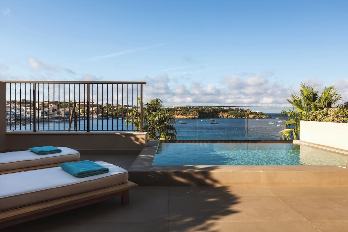 A rooftop pool with a view of the sea, lounge chairs, and a railing.