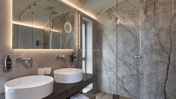 Un baño moderno con dos lavamanos, una cabina de ducha de vidrio y paredes de mármol.