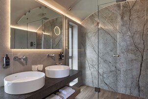 Un baño moderno con dos lavamanos, una cabina de ducha de vidrio y paredes de mármol.