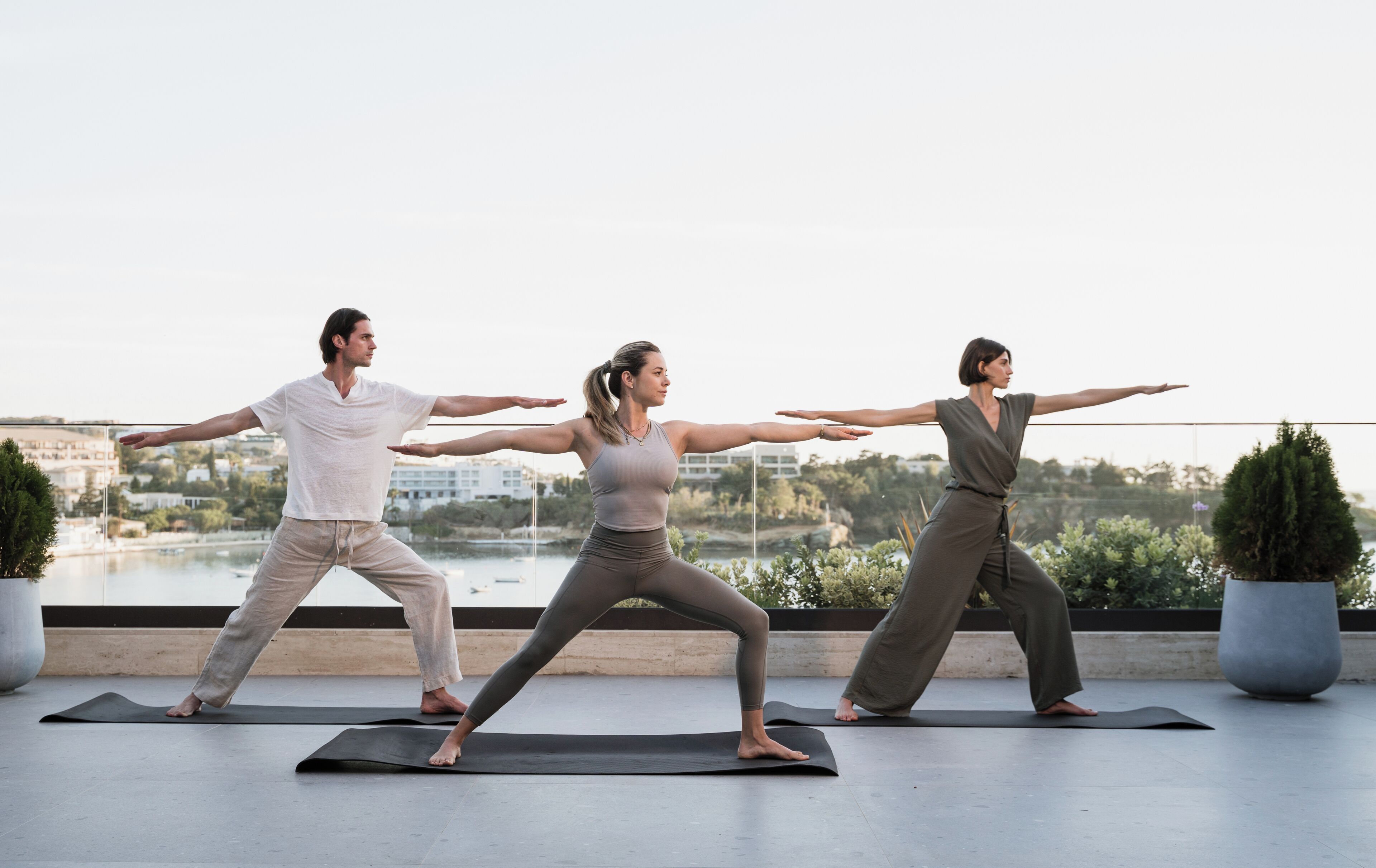 Drie personen beoefenen yoga op een dak met uitzicht over de stad.