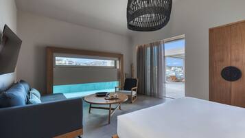 A modern hotel room with a bed, a sofa, a round table, and a chair. There is a large window with a view of the city and a door with a circular design.