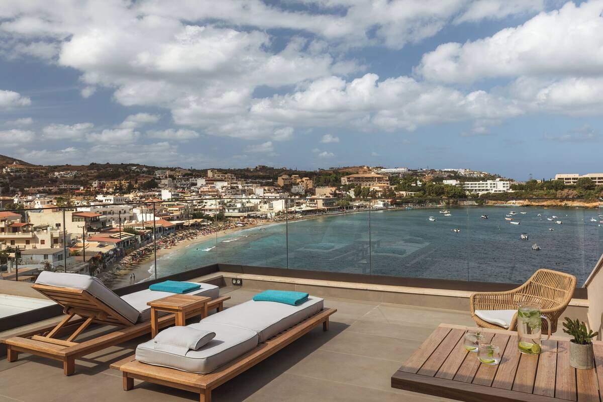 A rooftop terrace with lounge chairs and a view of a beach and sea.