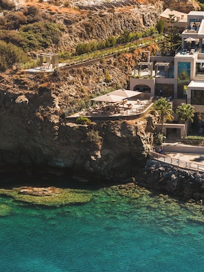 Un hotel costero con terraza exterior con vistas al mar, un acantilado rocoso y una vista despejada del océano.