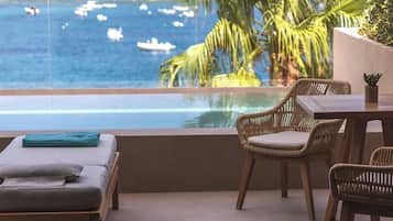 Een balkon met uitzicht op zee, rieten meubels en een tafeltje met een plant.