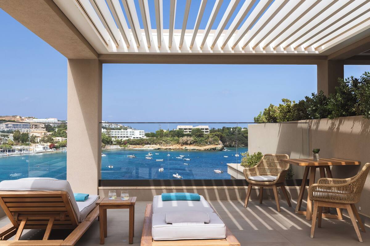 A balcony with a view of the sea, a sofa, a table, and two wicker chairs.