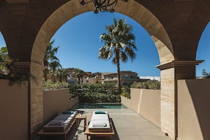A pool area with lounge chairs and a palm tree, framed by an arched structure. - Castello Infinity Suites - Adults Only (Malevizi)