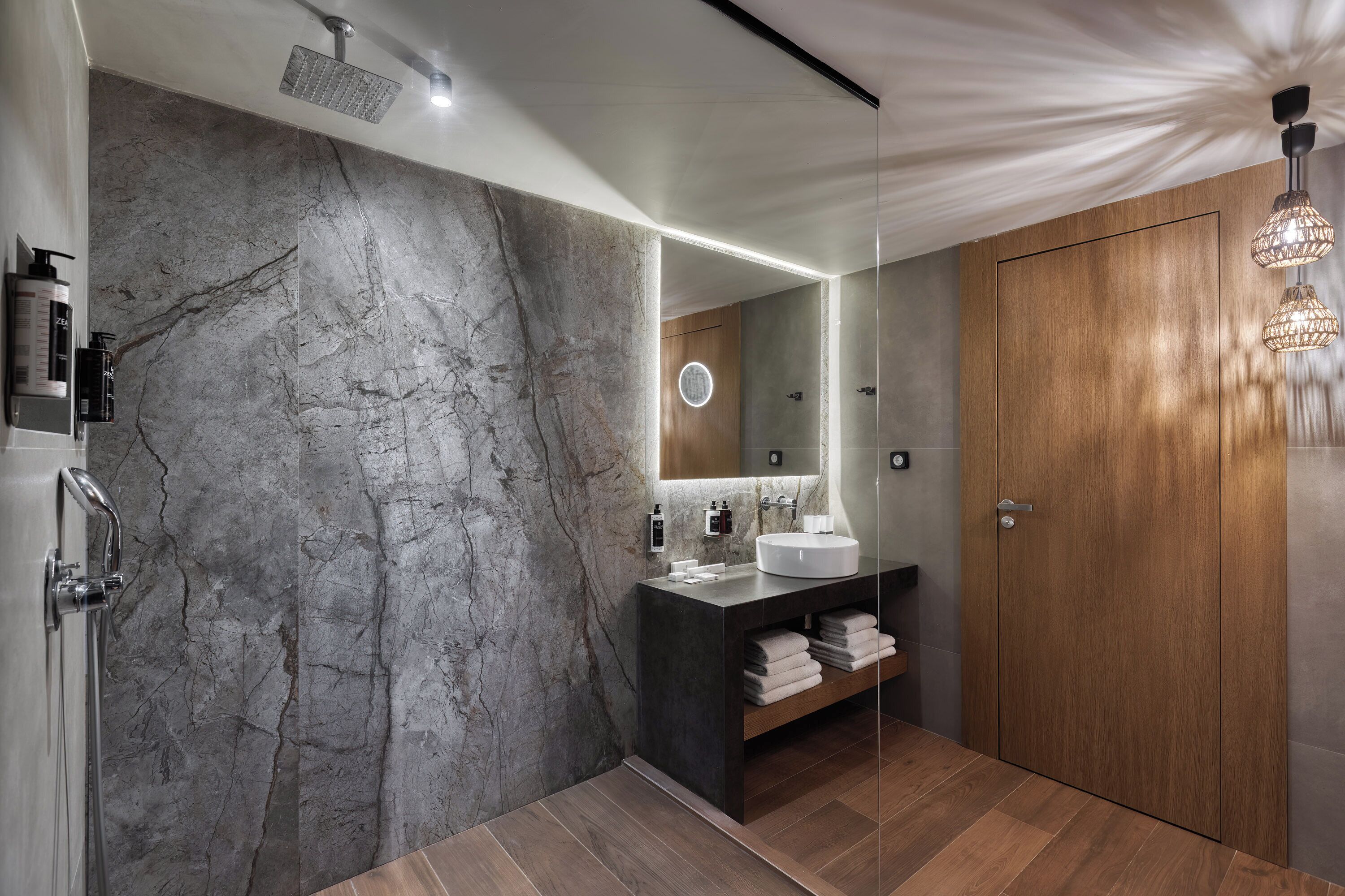 A modern bathroom with a marble wall, a wooden vanity, and a large mirror.
