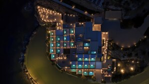 A modern hotel with multiple swimming pools, a beachside location, and a well-lit exterior.