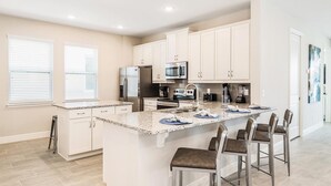 A modern kitchen with white cabinets, a granite countertop, stainless steel appliances, and a bar area with stools. - Perfect 5 Bedroom Villa on Encore Resort at Reunion, Orlando Villa 4516 (Orlando)