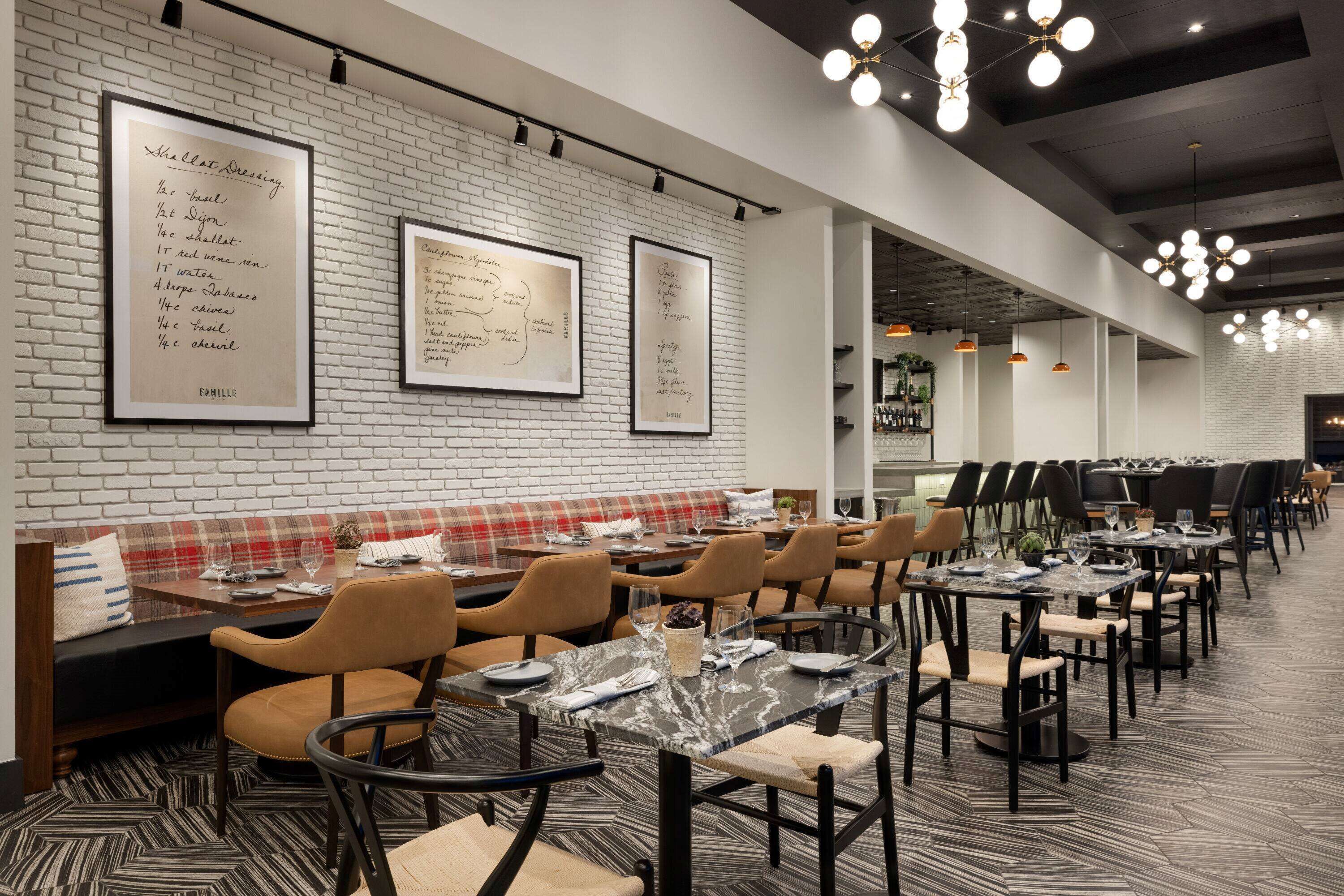 Um restaurante com parede de tijolos, quadros de menu e uma ampla área de refeições com mesas e cadeiras.