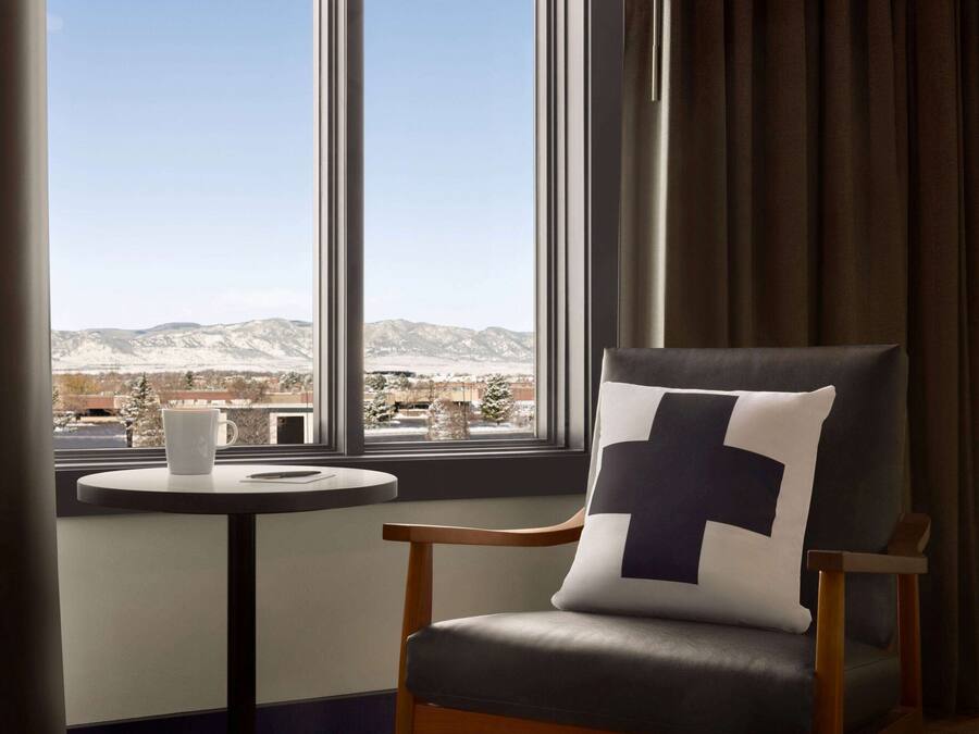 Une pièce avec vue sur les montagnes, grâce à de grandes fenêtres, une table ronde avec une tasse blanche et une chaise dotée d’un grand coussin.