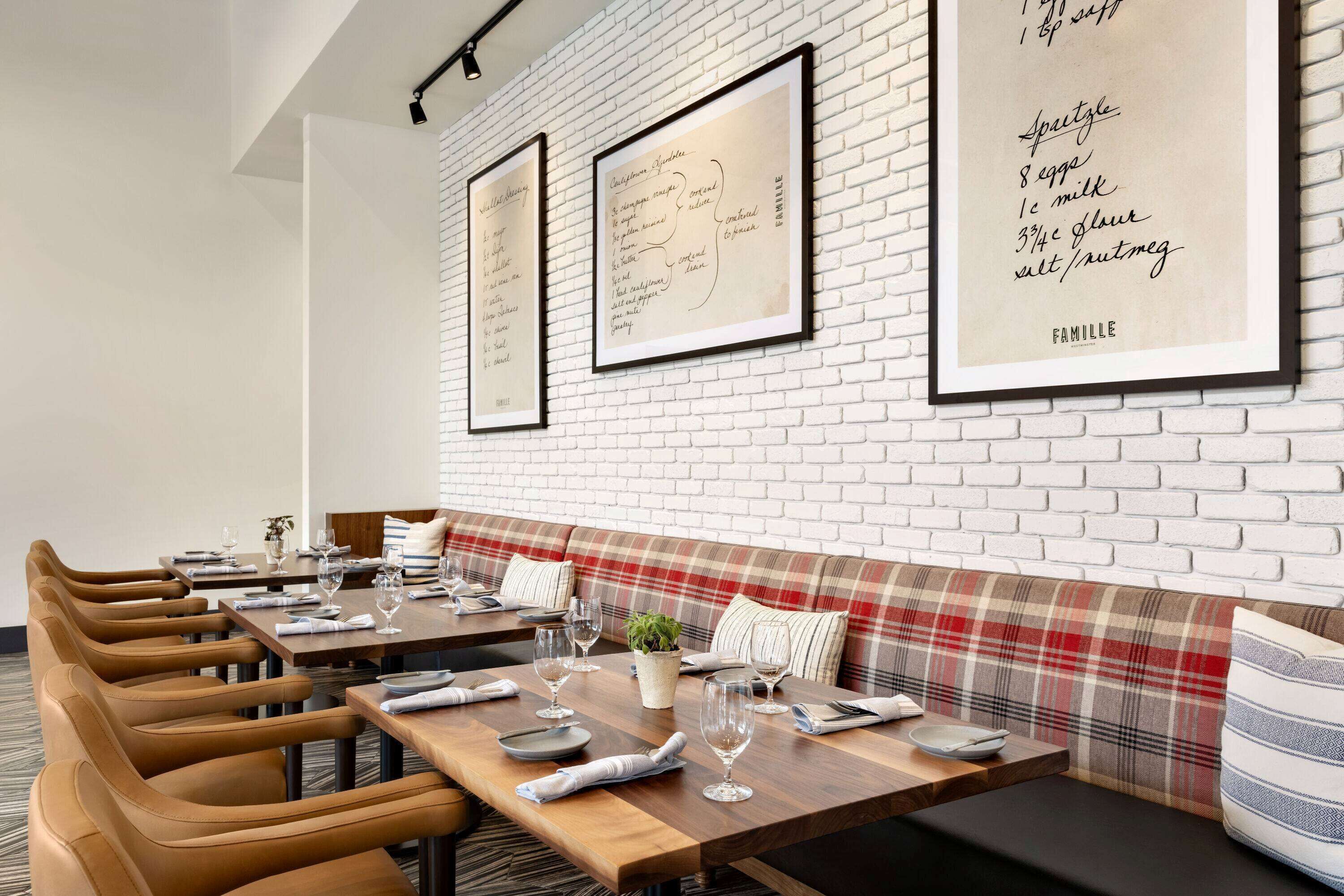 A restaurant interior with brick walls, framed menus, and a plaid bench.