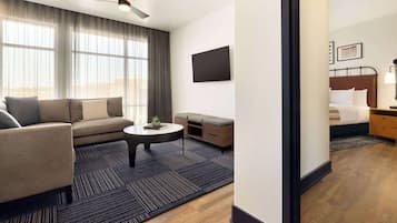 A modern hotel room with a sofa, a small coffee table, a TV, and a bed with a nightstand.