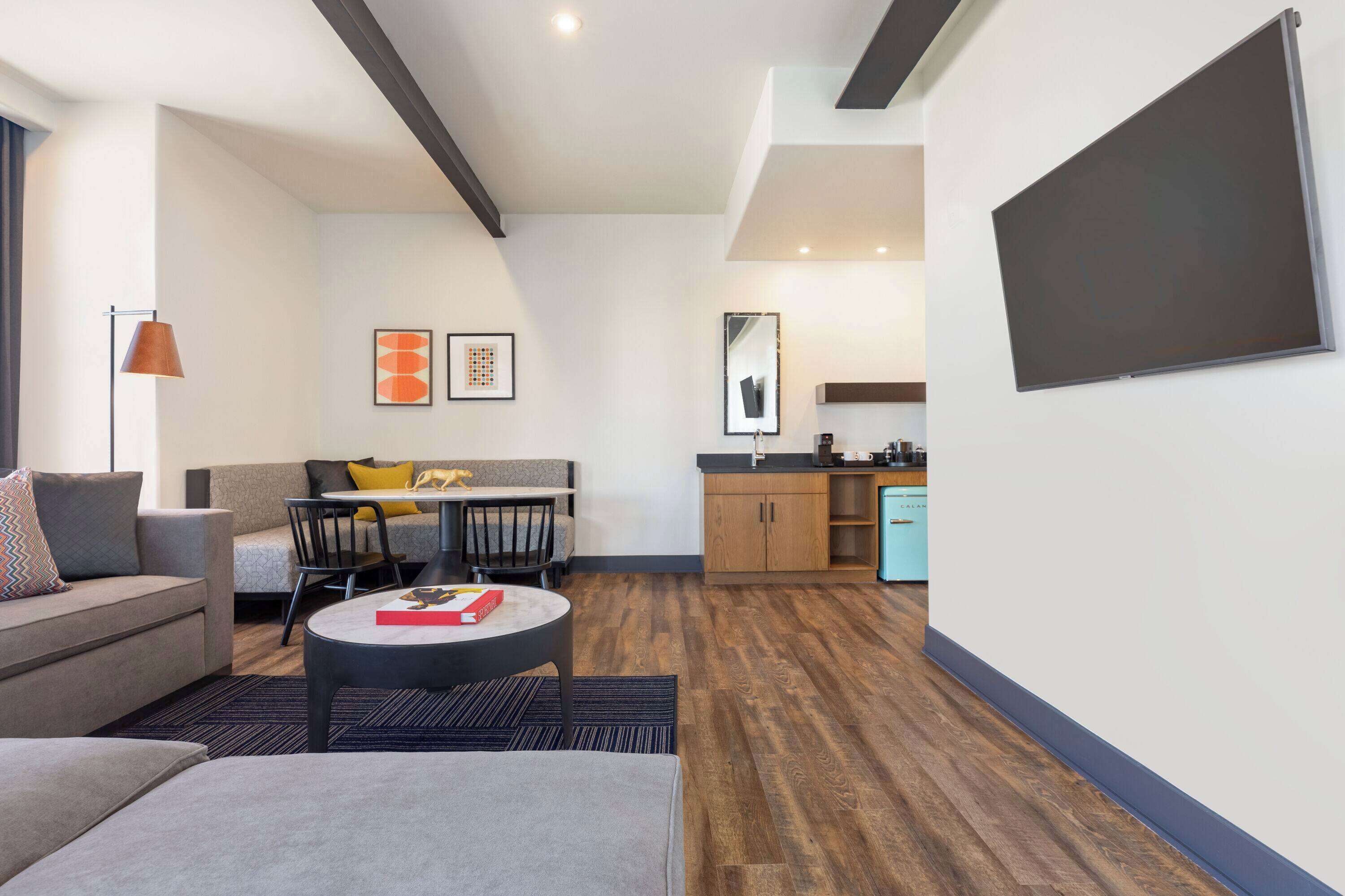 A modern living room with a sofa, a dining table, and a kitchen area with cabinets and a sink.