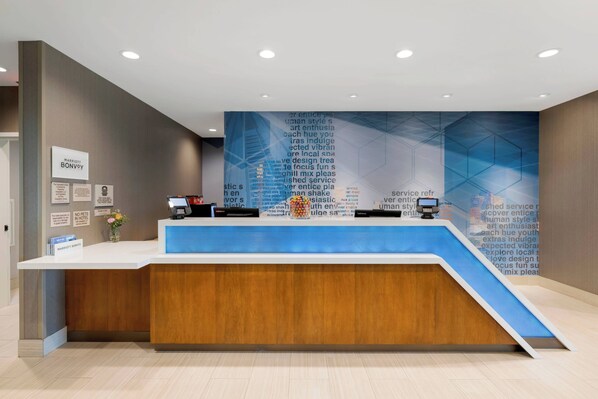 A modern hotel reception desk with a blue and white color scheme, a digital screen, and a wall with various words and phrases.
