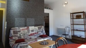 A living room with a sofa covered in newspapers, a wooden table with a teapot, a metal shelf, and a chair.