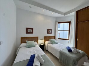 A hotel room with two beds, a window, and a door. - Sea front partment on Puerto Pollença Pinewalk, Kika (Pollensa / Pollença)