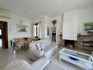 En stue med sofa, spisebord med stole, reol og pejs.