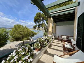 A balcony with outdoor seating, a view of the sea, and a tree.