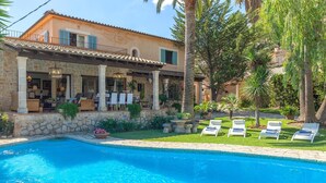 Un espace aménagé au bord de la piscine, avec des chaises longues et un bâtiment en pierre surmonté d’un toit en tuiles.