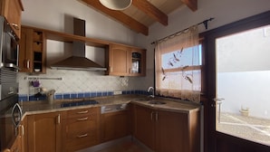 A kitchen with wooden cabinets, a stainless steel range hood, a tiled backsplash, and a window with a decorative curtain.