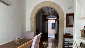A dining area with a wooden table and striped chairs, an arched doorway leading to a kitchen, and a tiled floor.