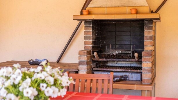 Ein Grill mit Backsteinofen im Freien, bedeckt mit einer roten Tischdecke, mit einem Holzstuhl davor.