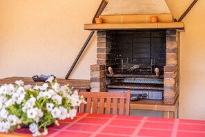 Un barbecue extérieur en briques, avec une nappe rouge et une chaise en bois devant.