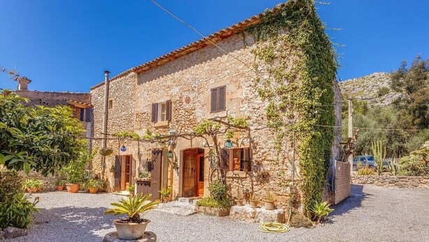 A stone building with a rustic appearance, featuring a courtyard with potted plants and a gravel path. - Charming stone clad family villa with pool La Font (Pollensa / Pollença)