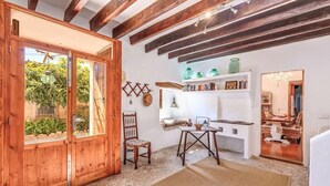 A rustic interior with exposed wooden beams, a wooden door, a dining area with a table and chairs, and a shelf with books and decorative items. - Charming stone clad family villa with pool La Font (Pollensa / Pollença)