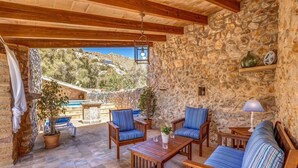 A stone-walled patio with wooden furniture, a hanging lantern, and a view of a mountainous landscape. - Charming stone clad family villa with pool La Font (Pollensa / Pollença)