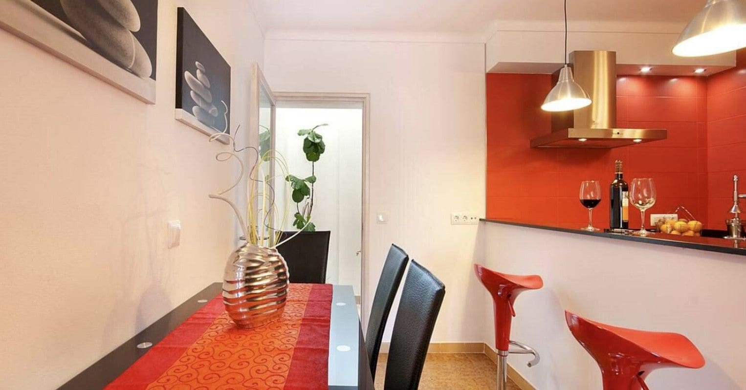 Et spiseområde med et bord dækket til to personer, en vase med planter og en bagplade med røde og hvide fliser.