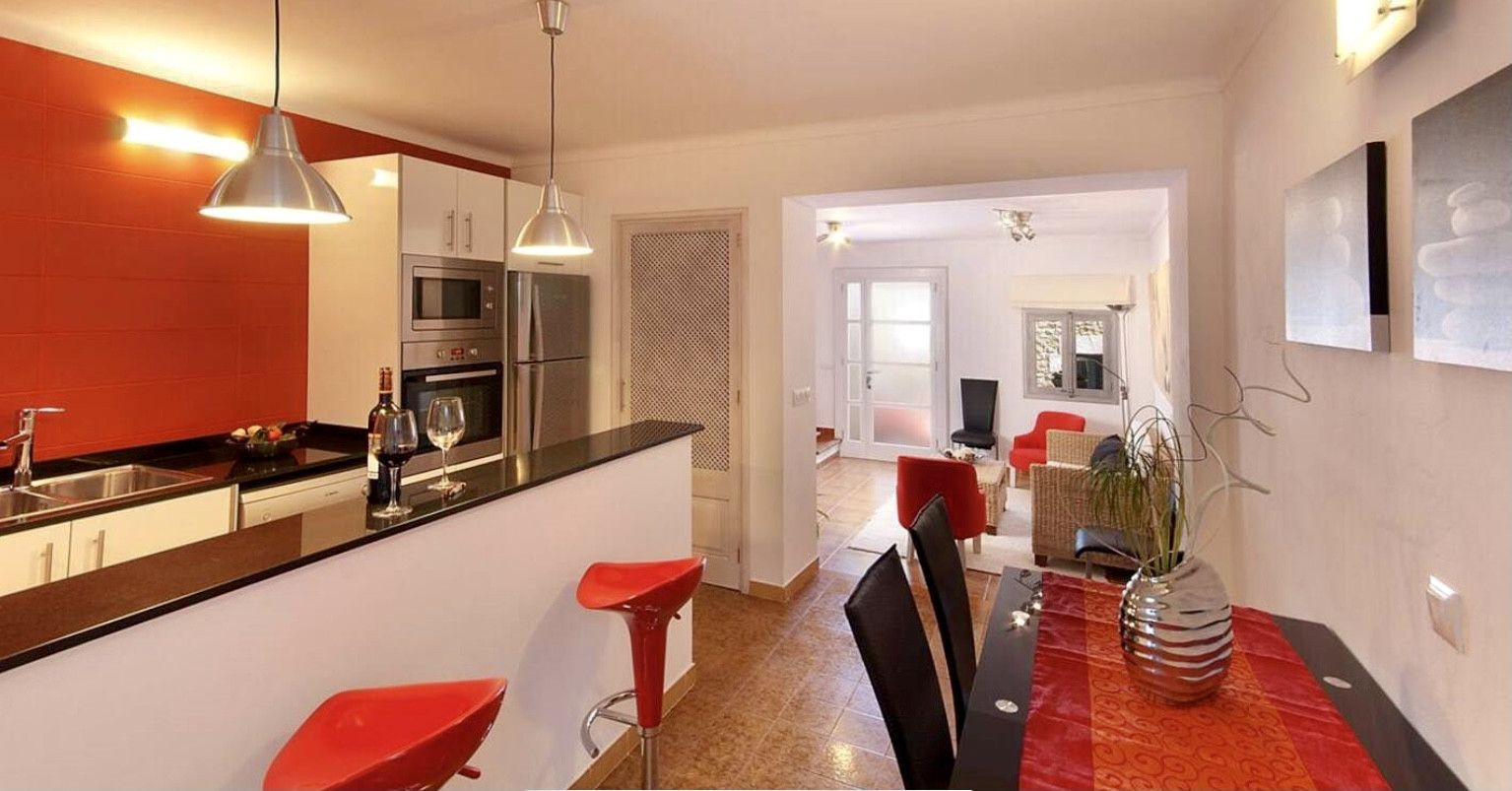 A modern kitchen with a dining area, red bar stools, and a dining table with a vase.